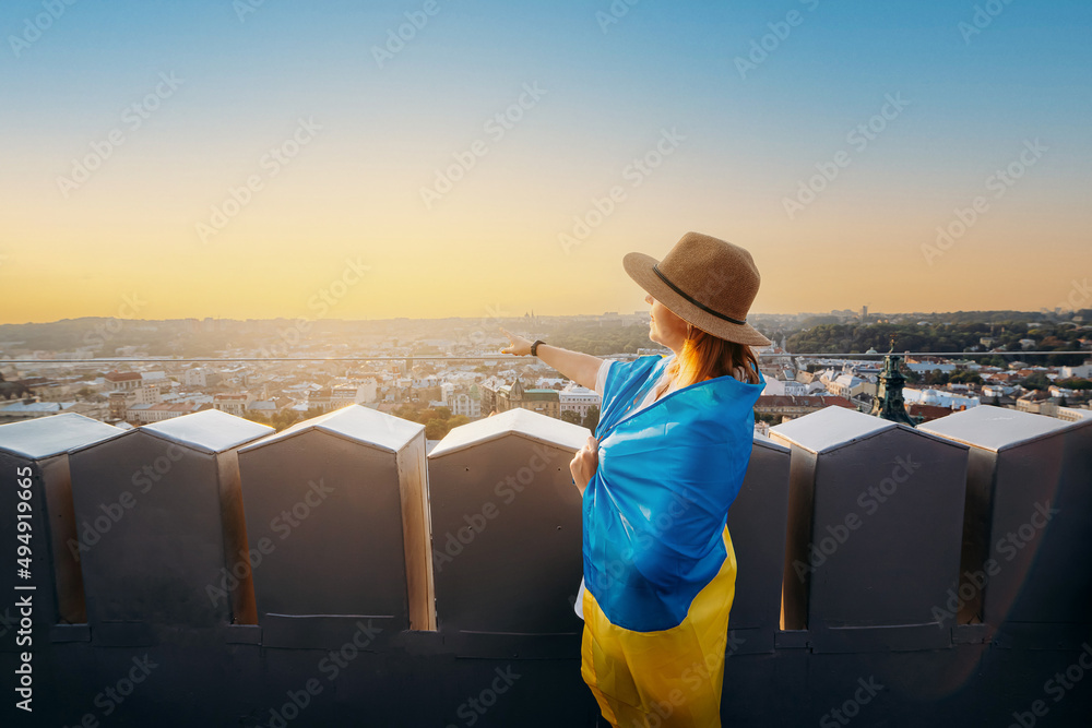 Fototapeta premium A woman stands with the national Ukrainian flag and waving it praying for peace at sunset in Lviv..A symbol of the Ukrainian people, independence and strength. Pray for Ukraine.