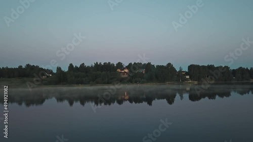 Mist over the river in the early morning dawn. A group of young people resting and singing songs on the shore, woods and countryside in the background 