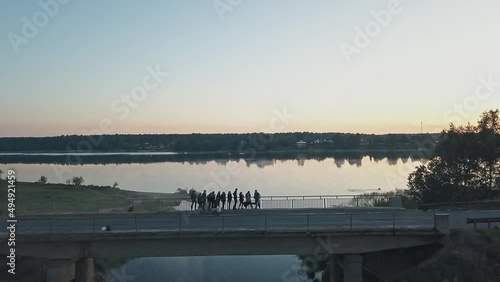 Young people on a lonely road on a bridge near a church and river on a foggy morning at dawn. River, forest, fog, village