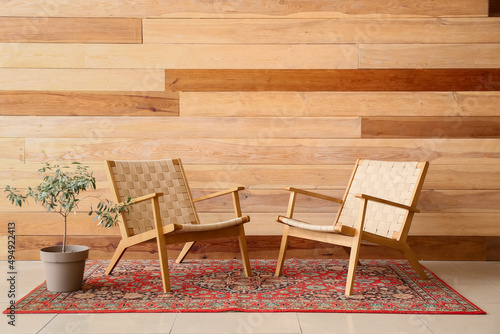 Armchairs with houseplant and vintage carpet near wooden wall