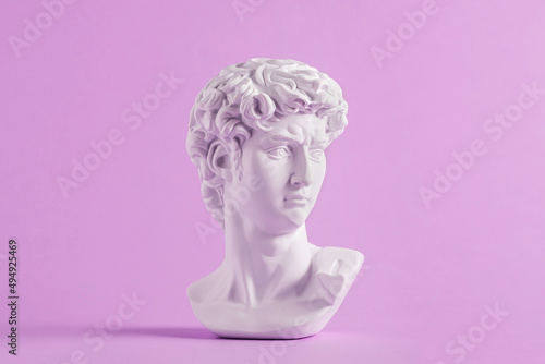 Ancient statue is head of David on purple background.