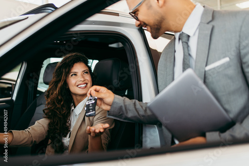 Happy and beautiful middle age business woman buying new car at showroom. A nice seller helps her make the right decision. He gives her the car keys.