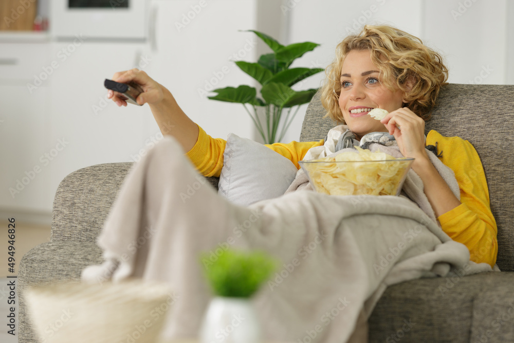 woman with bowl of potato chips watching tv on sofa