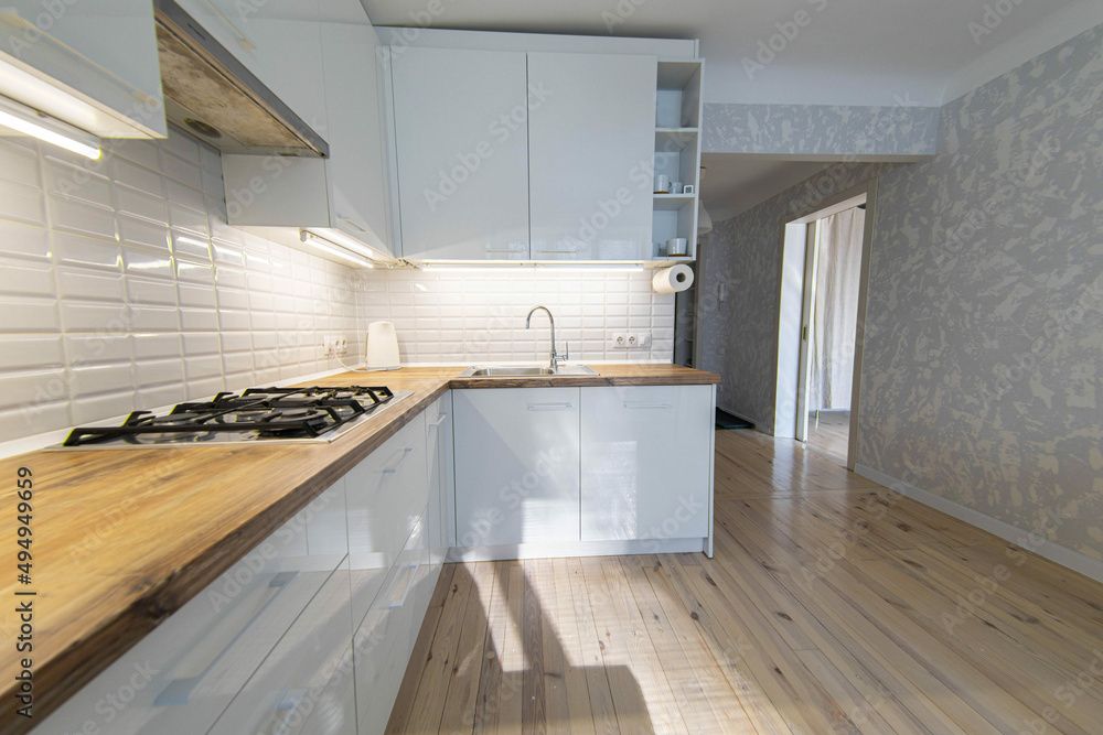 Fototapeta premium interior of cozy small kitchen with wooden floor, white cabinets and solid wood worktop.