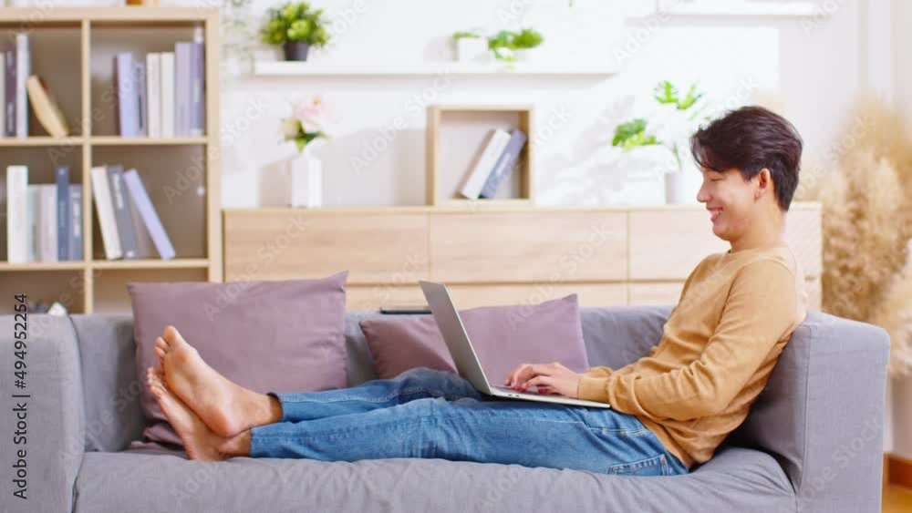 Entrepreneur handsome business asian man wear shirt lying on couch working online with computer laptop on smile and happiness at home office.Small Business Startup Concept