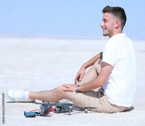Young man sitting on the ground near drone and drone remote controller. A smiling man in a sports suit on a sunny summer day.