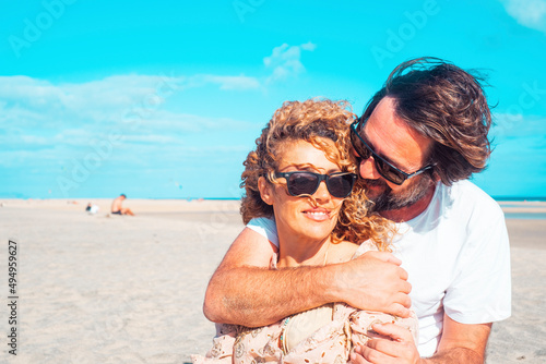 Summer love couple man and woman hugging in relationship with sand beach and ocean in background. Holiday vacation leisure lifestyle people in outdoor. Two adults embracing and smile enjoying