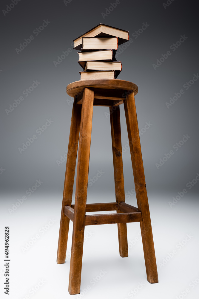 stack of books on wooden stool on grey background. stack of books on wooden stool on grey background.