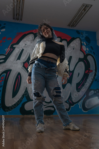 Female dancer in activewear squatting on the floor of modern dance studio and looking at you