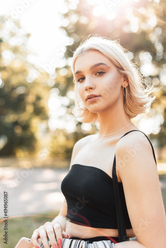 Bright portrait of fashion beautiful woman with short hair in black summer tank top walks in the park on sunny day