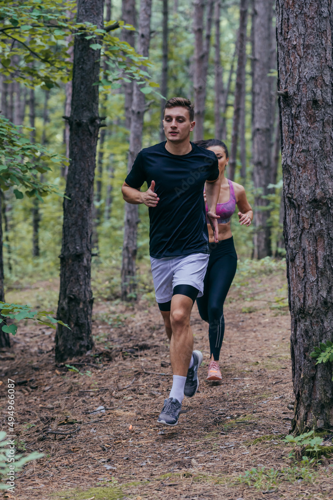 Young athletic couple is running outdoors in the wooded forest area