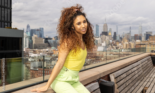 Smiling mixed race woman with black and brown curly hair wearing summer fashion outside with cityscape view of New York City.
