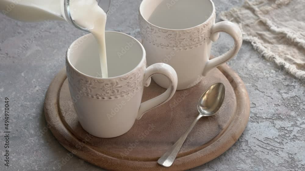 Pouring fresh kefir from a glass jug into two ceramic cups Pouring fresh kefir from a glass jug into two ceramic cups