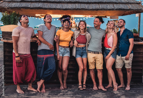 Happy young millennials having fun and laughing at kiosk in the evening - Group of happy multiracial friends dancing at sunset beach party in summer vacation - Youth lifestyle and nightlife concept photo
