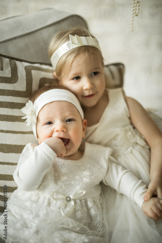 two beautiful sisters sit on an armchair in an embrace