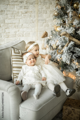 two beautiful sisters sit on an armchair in an embrace in holiday christmas