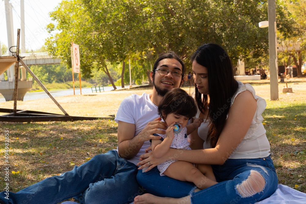 © Antonio Tanaka - Young Hispanic parents playing with their one year old baby in a park