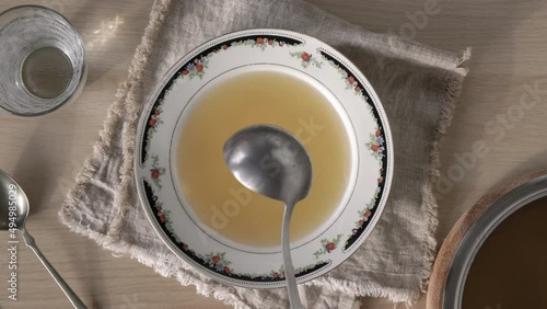 Pouring homemade bone broth into a plate with a ladle, top view