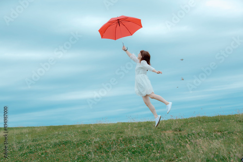 草原で傘を持ってジャンプする女性