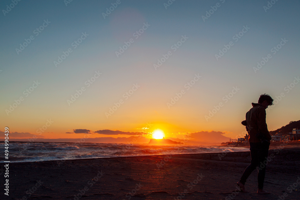 夕暮れの砂浜を歩く男性