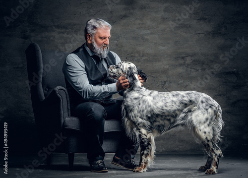 Elderly man dressed in elegant clothing posing on armchair with his dog