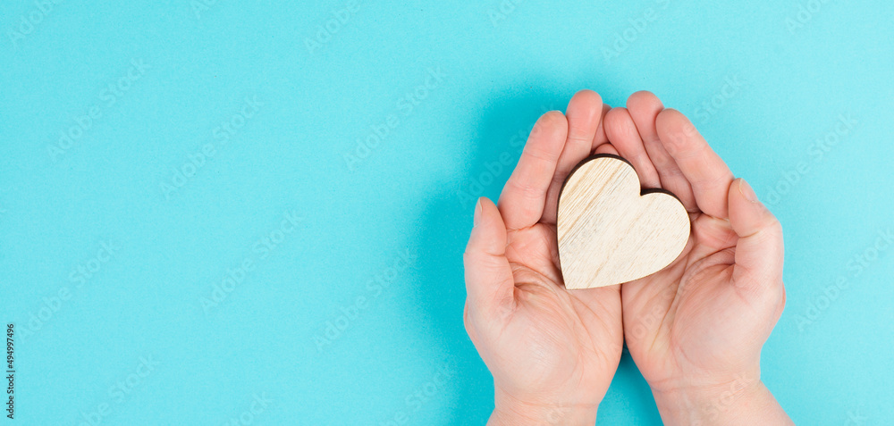 Woman is holding a red heart in her hand, blue colored background, copy space, love and charity symbol, hope concept
