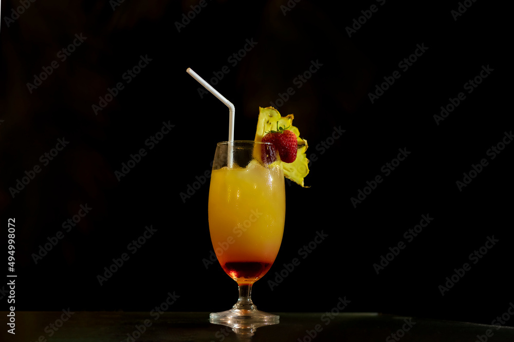 Alcoholic, tropical drink, decorated with strawberries and a slice of pineapple. Sunrise cocktail in a tall glass on a black background. Alcoholic, tropical drink, decorated with strawberries and a slice of pineapple. Sunrise cocktail in a tall glass on a black background.