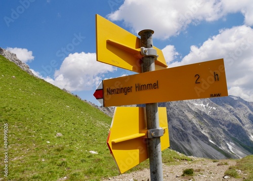 Yellow signpost indicating way to Nenzinger Himmel, beautiful Austrian Alps in the background. photo