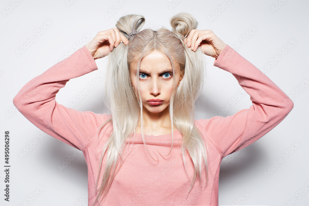 Cute and funny blonde girl holding she's hair buns on white studio background. Cute and funny blonde girl holding she's hair buns on white studio background.
