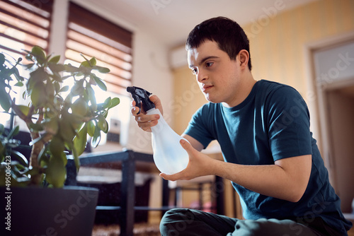 Canvas Print Man with down syndrome taking care of houseplants and spraying them with water