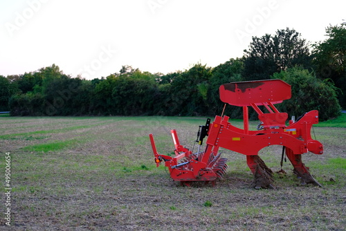 red agricultural machinery, plow, harrow for tillage in the field after harvest, green trees in the background, modern crop cultivation concept