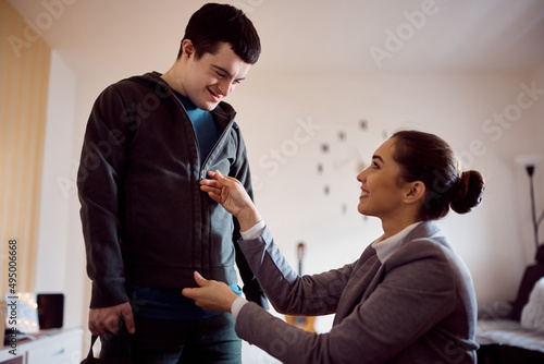 Happy down syndrome man zipping his jacket with help of tutor at home. photo