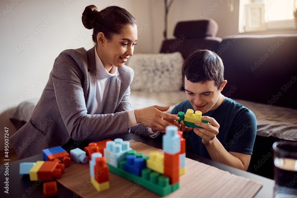 Happy man with down syndrome and his psychologist play with toy blocks at home. Happy man with down syndrome and his psychologist play with toy blocks at home.