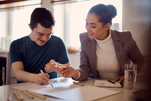 Young happy down syndrome man having special education class with his psychologist at home.