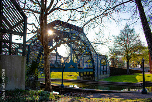 Fotografija Sunlight Peeks through the Metal Arch of a Bridge Crossing a Stream in the Louis