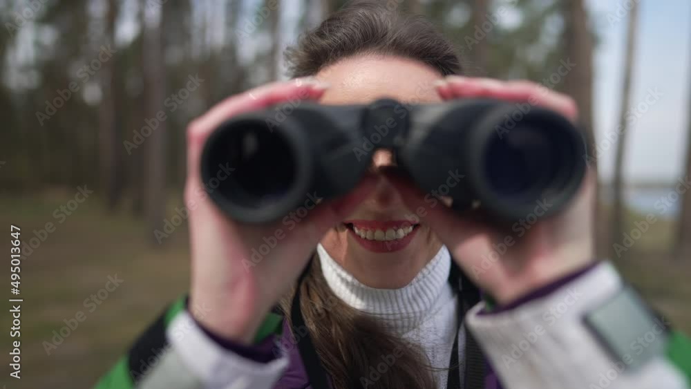 Front view smiling woman using binoculars looking at camera standing in forest. Happy confident satisfied Caucasian tourist travelling outdoors enjoying vacations. Slow motion Front view smiling woman using binoculars looking at camera standing in forest. Happy confident satisfied Caucasian tourist travelling outdoors enjoying vacations. Slow motion