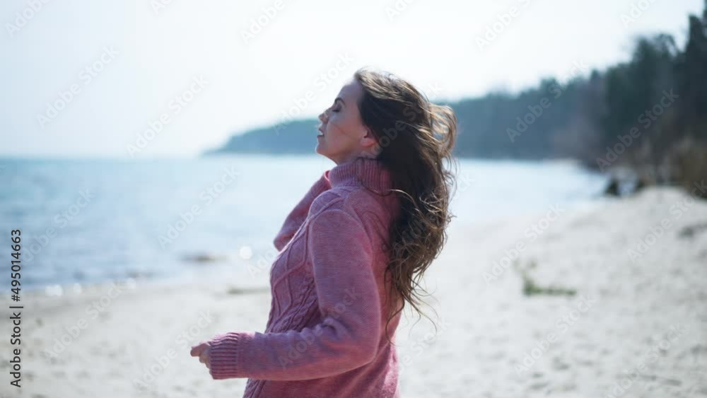 Back view beautiful scared woman running in slow motion turning looking back. Frightened Caucasian lady in pink knitted dress escaping from danger on sandy beach in sunshine. Panic and scare
