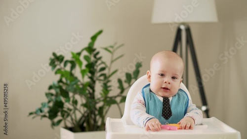 mom Mother feed young baby in white feeding up high chair, first supplement vegetable puree Happy smiling kid eat for the frst time, child with dirty face, little infant boy eating porridge nutrition photo