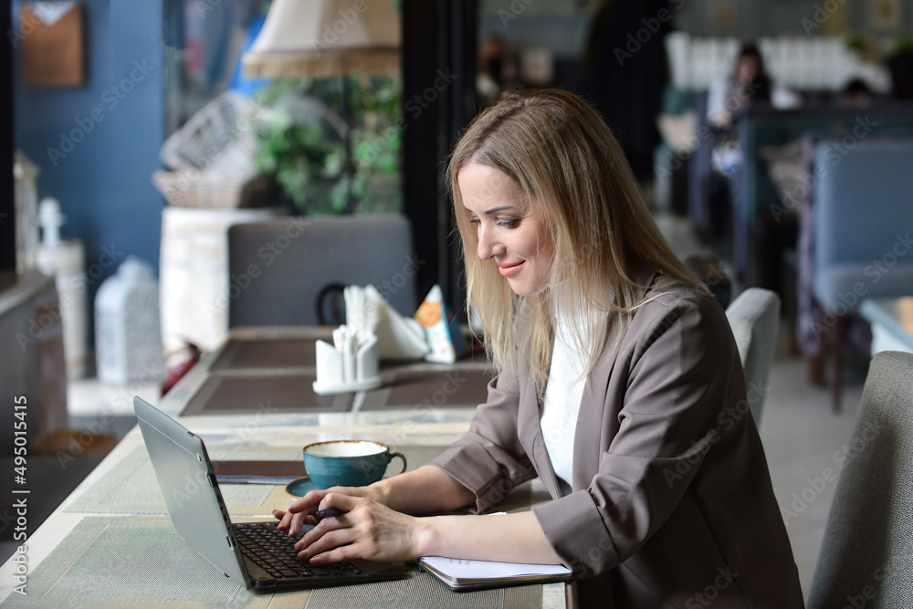 a business young beautiful woman sits at a table in a cafe waiting for an order, in front of her is a laptop in which she works online a business young beautiful woman sits at a table in a cafe waiting for an order, in front of her is a laptop in which she works online