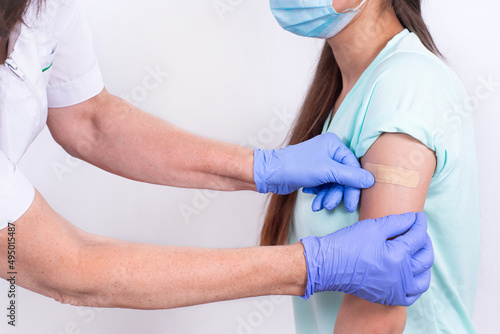 Doctor or nurse glues bandage on patient's shoulder after an injection or vaccination. Close-up. Vaccination against flu, pandemic coronavirus. Mandatory prevention of people for immunity from virus.
