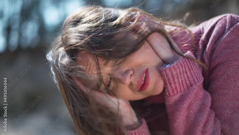Headshot portrait of desperate frustrated Caucasian woman holding head in hands thinking sitting outdoors. Close-up of brunette depressed lady in sunshine outdoors. Slow motion Headshot portrait of desperate frustrated Caucasian woman holding head in hands thinking sitting outdoors. Close-up of brunette depressed lady in sunshine outdoors. Slow motion