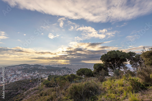 Picturesque landscape of Barcelona from the hill in the early morning. Sunbeams through the clouds. Dramatic sky over the city. Autumn in Barcelona, Spain.