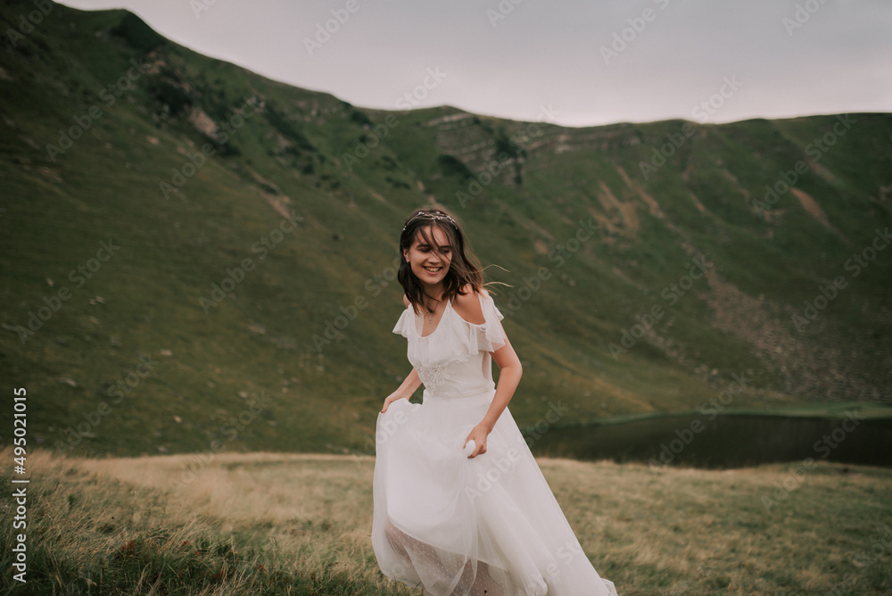Happy bride in white wedding dress smiling against the backdrop of mountains.