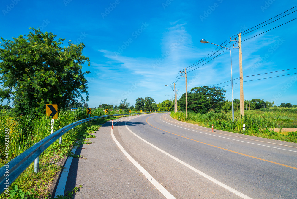 Beautiful curved country asphalt road, Thailand in sunny day blue sky background. Transportation and nature concept.