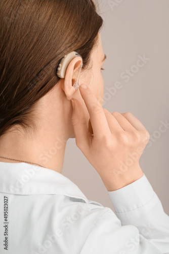 Young woman with hearing aid in her ear on grey background, closeup