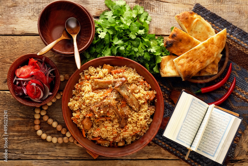 Bowl with tasty Asian pilaf, flatbread and Quran on table photo