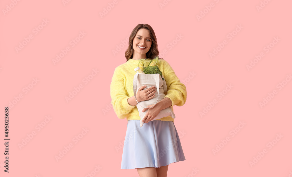 Young woman holding eco bag with food and drink on pink background Young woman holding eco bag with food and drink on pink background