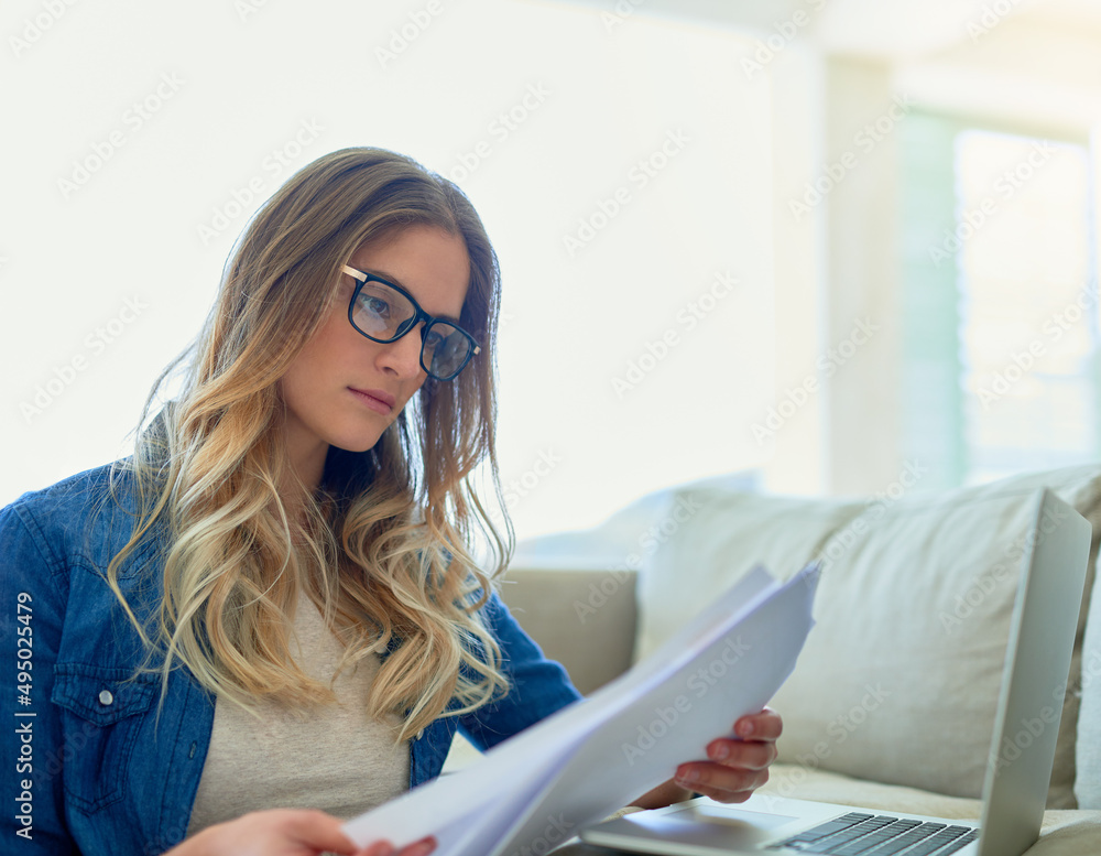 Working over the weekend. Shot of an attractive young woman reading paperwork while working at home. Working over the weekend. Shot of an attractive young woman reading paperwork while working at home.
