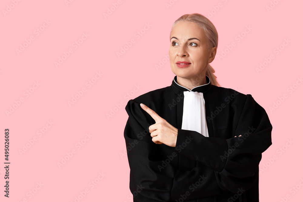 Mature female judge in robe pointing at something on pink background Mature female judge in robe pointing at something on pink background
