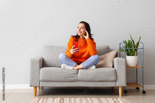 Fotografía Beautiful young woman with mobile phone resting on couch at home